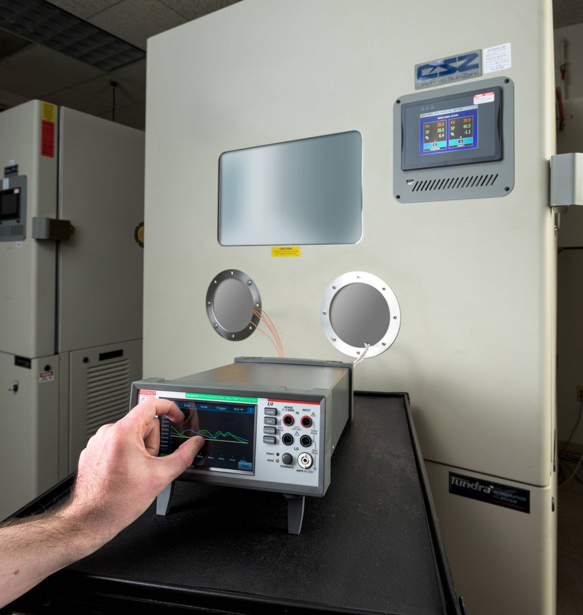 Eine Person bedient ein technisches Gerät mit einem Bildschirm, das an eine größere Maschine mit runder Öffnung angeschlossen ist.