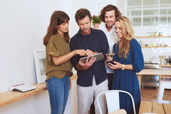 Eine Gruppe von vier Personen steht in einem modernen Büro und betrachtet gemeinsam ein Tablet. Sie wirken konzentriert und interessiert.