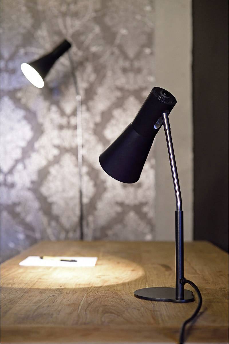 Zwei schwarze Tischlampen auf einem Holztisch; eine leuchtet auf ein Blatt Papier, die andere strahlt indirekt gegen die Wand.