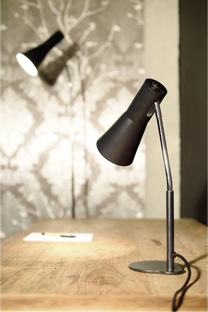 Schwarze Tischlampe auf Holzschreibtisch, im Hintergrund unscharfe stehende Lampe. Beige Tapete mit dezentem Muster.