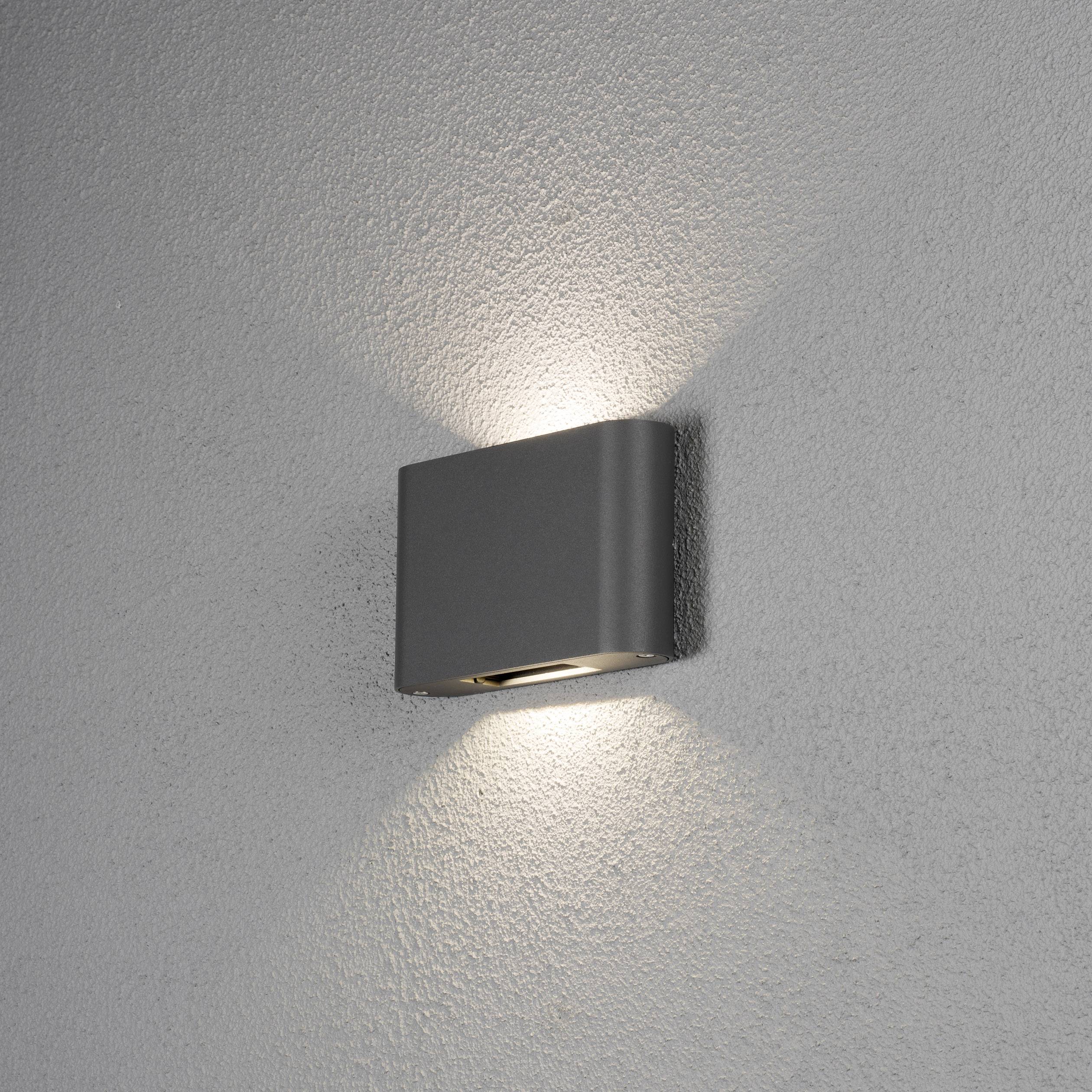 Wandlampe mit rechteckigem, grauem Gehäuse. Die Beleuchtung strahlt nach oben und unten und erzeugt ein symmetrisches Lichtmuster an der Wand.