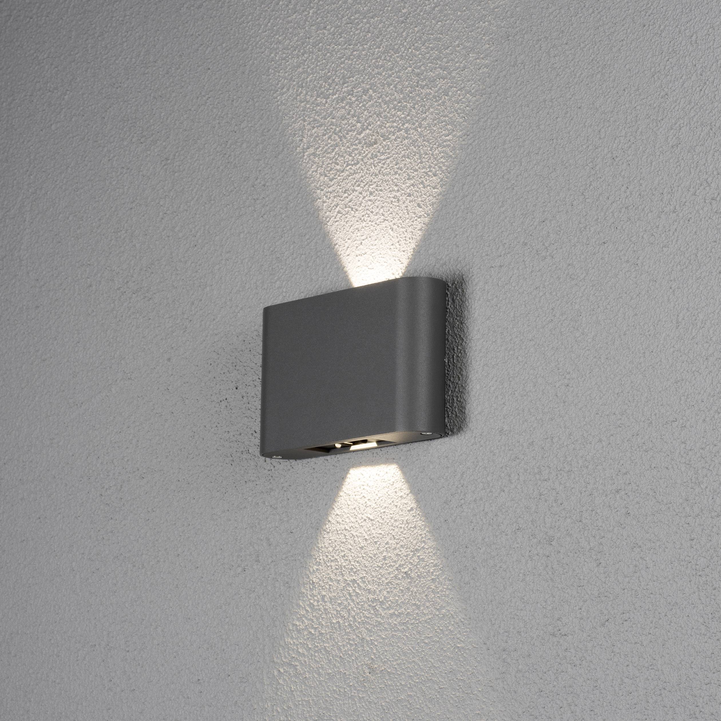 Wandleuchte mit modernem Design strahlt nach oben und unten, erzeugt ein sanftes, fokussiertes Lichtmuster auf grauer Wand.