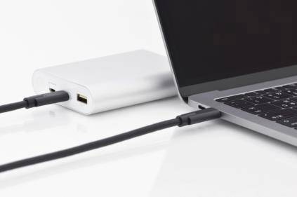 Ein Laptop wird von einer Powerbank mit Strom versorgt. Ein Kabel verbindet die Powerbank und den Laptop auf einem weißen Hintergrund.