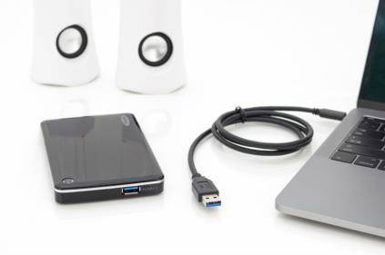 Externe Festplatte mit USB-Kabel, neben Laptop und Lautsprechern auf einem weißen Tisch.