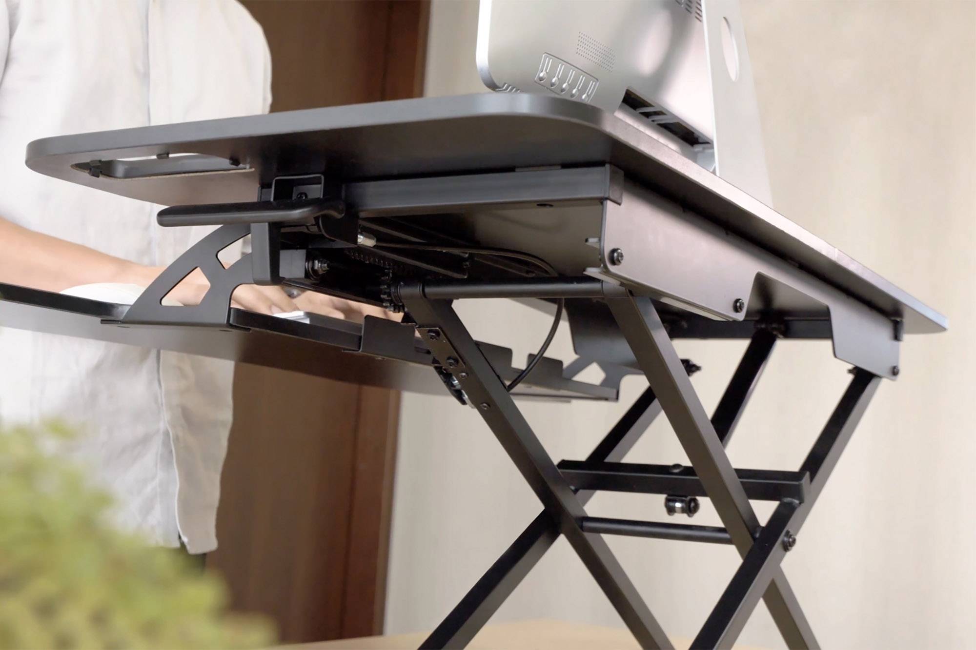 Ein höhenverstellbarer Schreibtisch mit Laptop, Person steht und tippt; zeigt ergonomische Arbeitsplatzlösung.