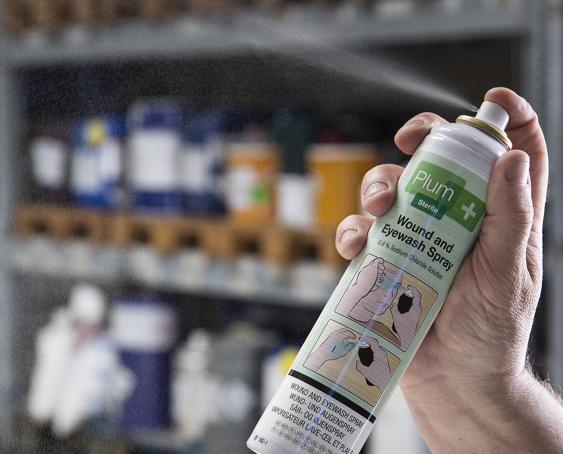 Eine Hand hält eine Sprühdose mit der Aufschrift 'Plum Wound and Eyewash Spray'. Im Hintergrund sind verschwommene Regale zu sehen.