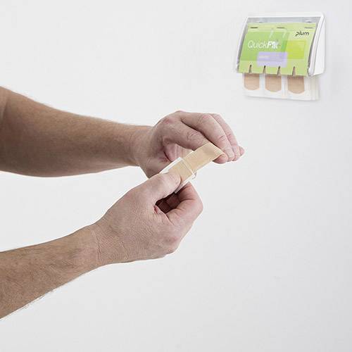 Eine Person legt ein Pflaster auf den Finger, vor einer Wand mit Pflasterspender.