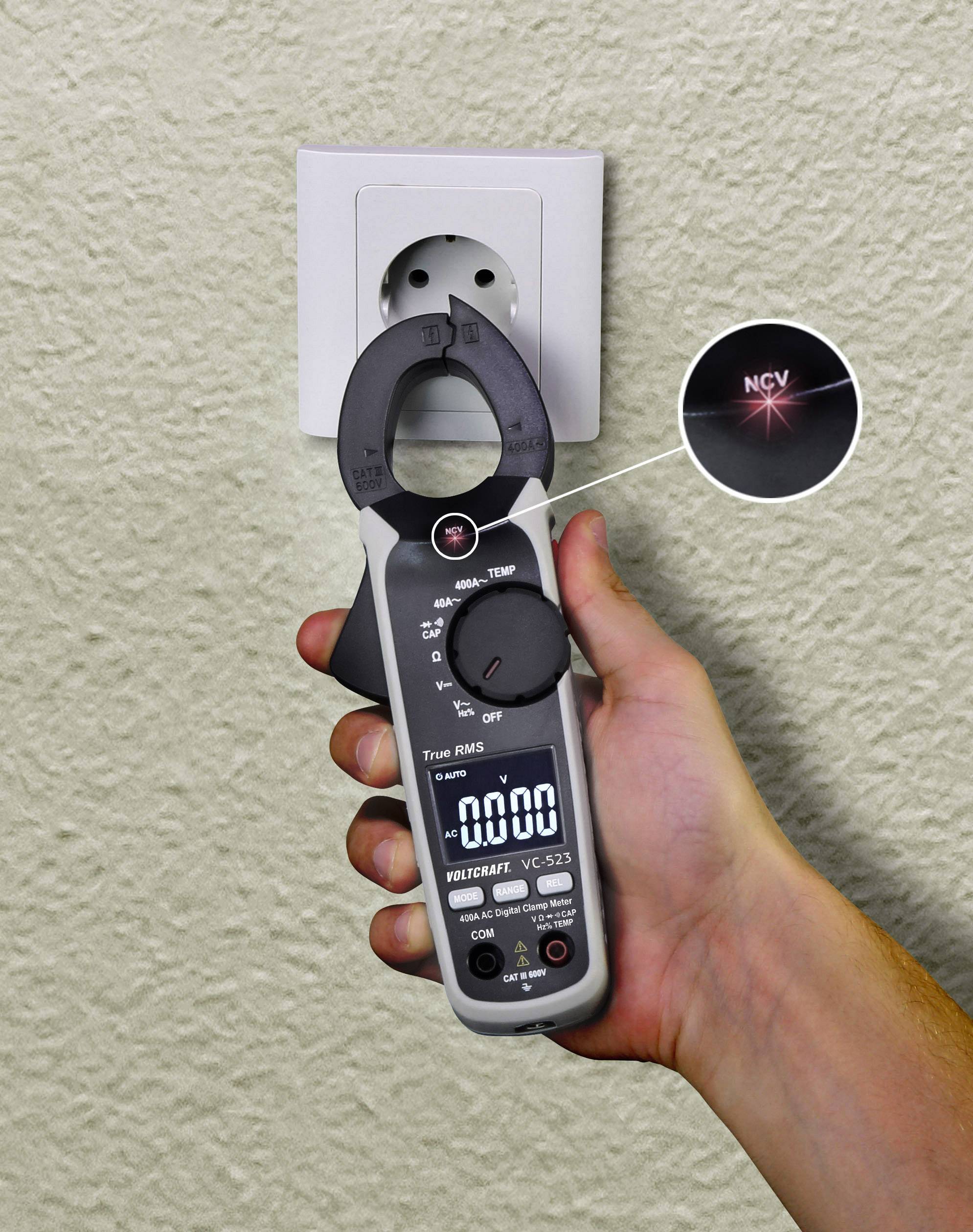 Eine Person hält ein digitales Multimeter vor einer Steckdose. Das Gerät misst Spannung und zeigt '0.000' auf dem Display an.