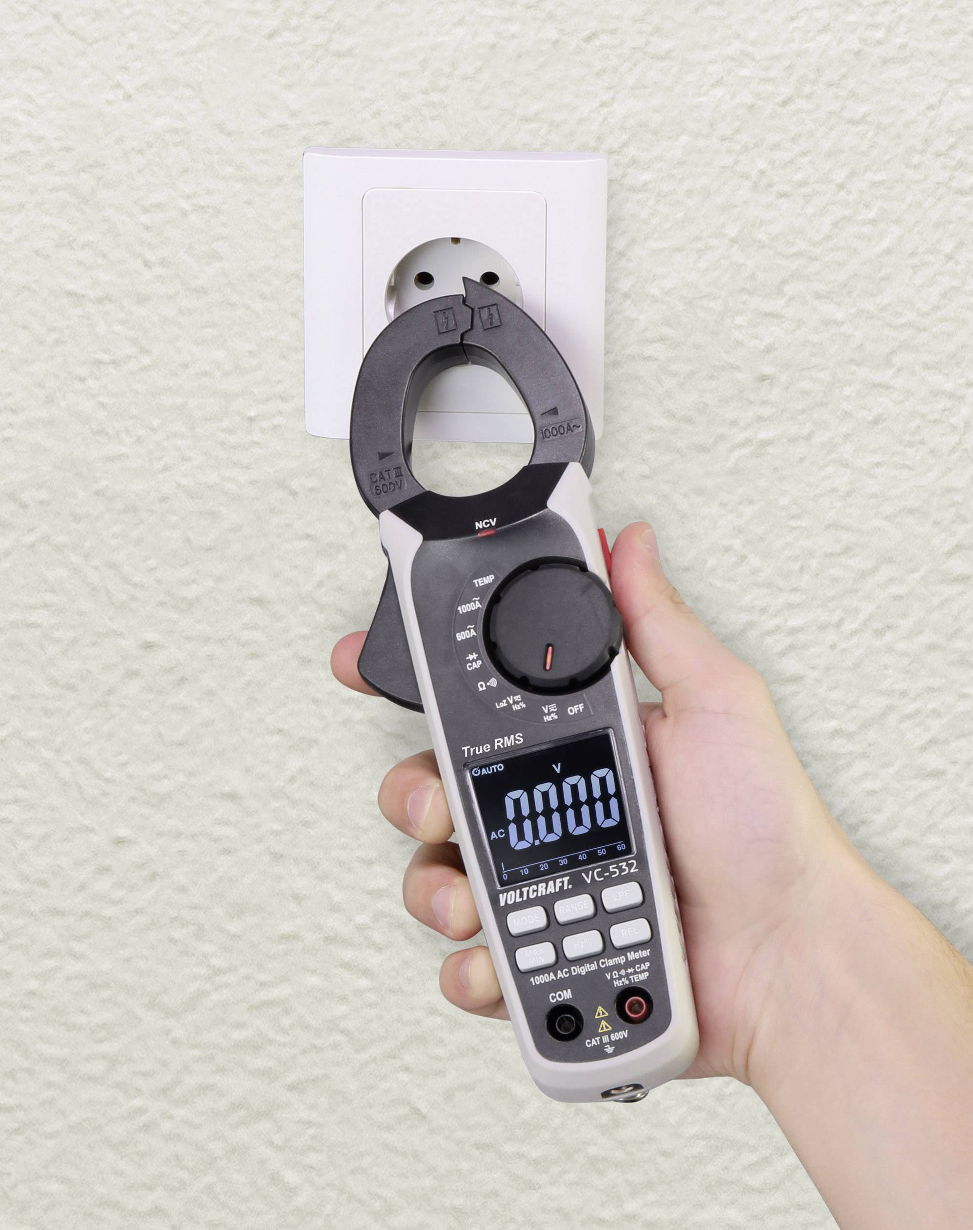 Eine Hand hält ein digitales Multimeter neben einer Steckdose, zeigt '0,000' auf dem Display, bereit zur Spannungsmessung.