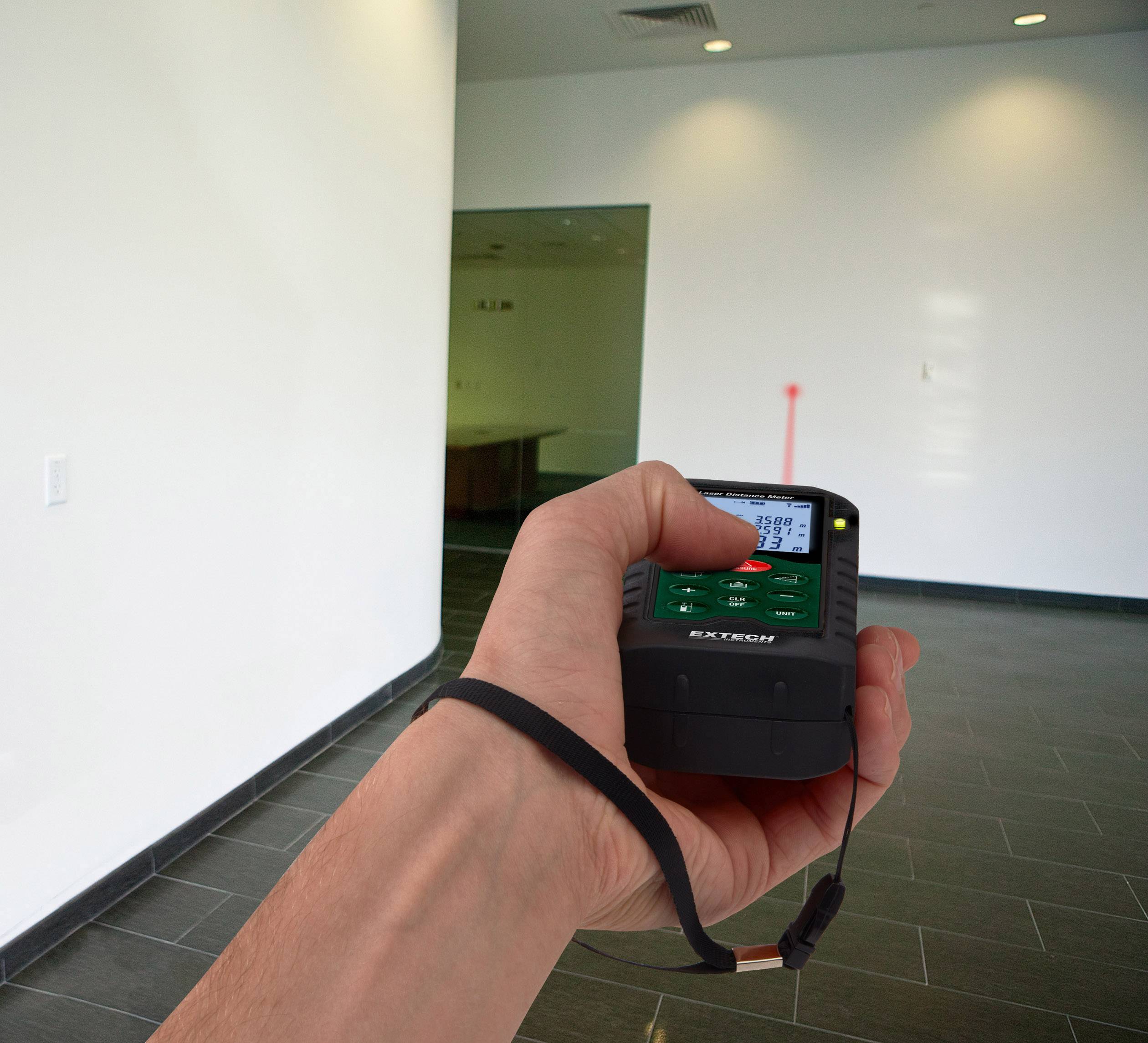 Eine Hand hält ein Laser-Entfernungsmesser in einem leeren Raum; rote Ziellinie zeigt gemessene Entfernung an.