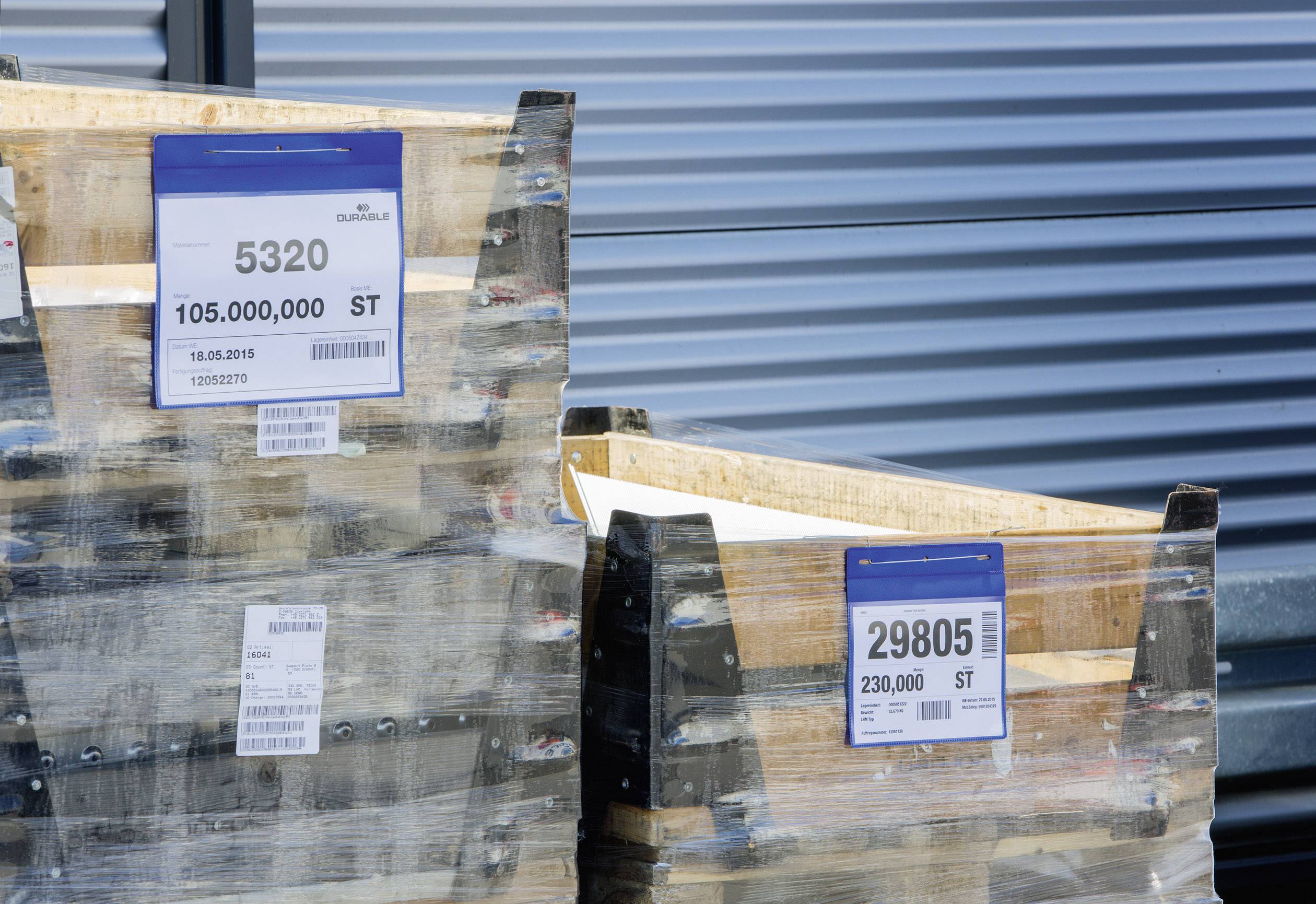 Zwei Holzpaletten vor einem Gebäude. Aufkleber zeigen Nummern: '5320' und '29805' mit Mengenangaben.