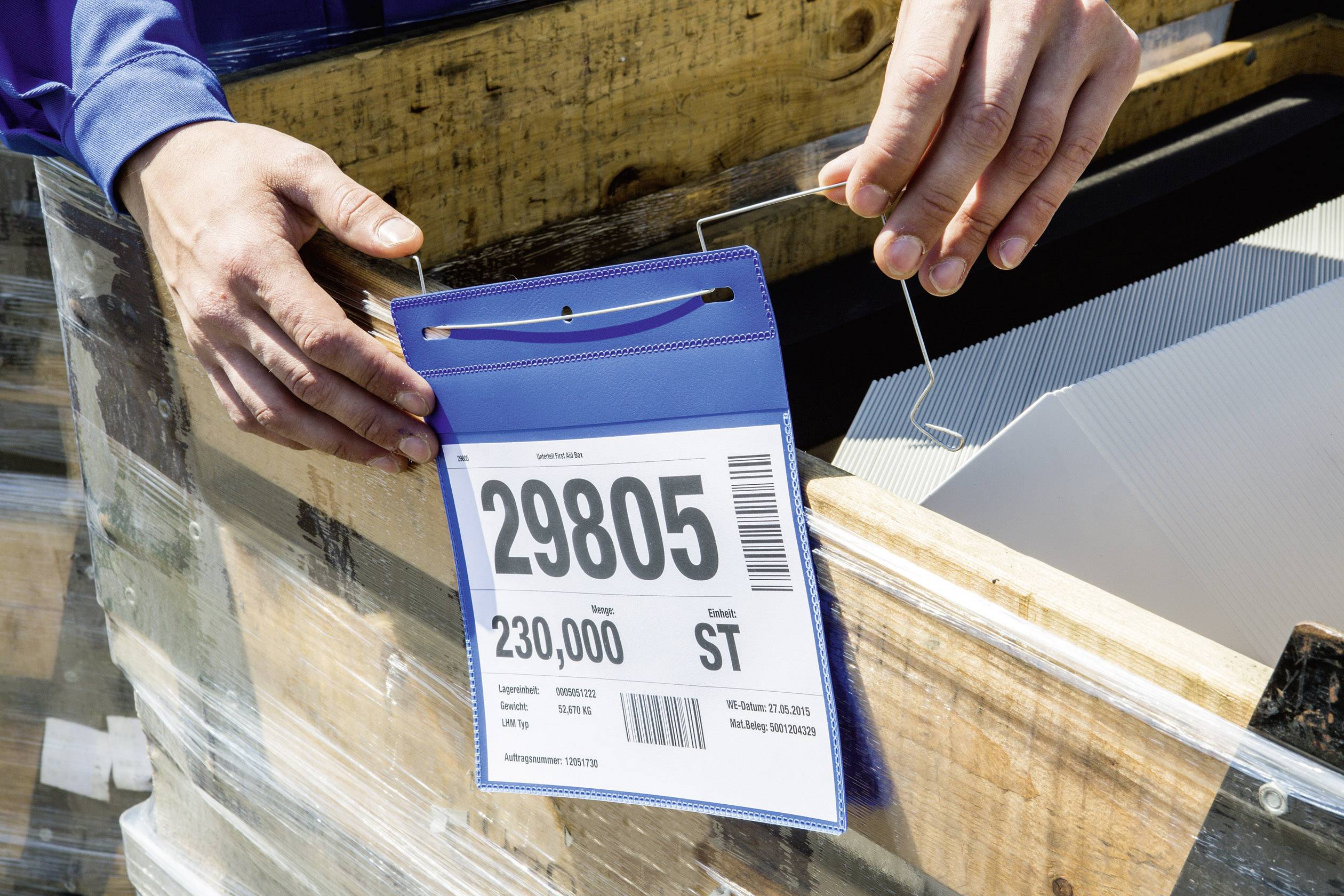 Eine Person hält ein Schild mit der Zahl '29805' und dem Text '230,000 ST', befestigt an einem Holzkasten.