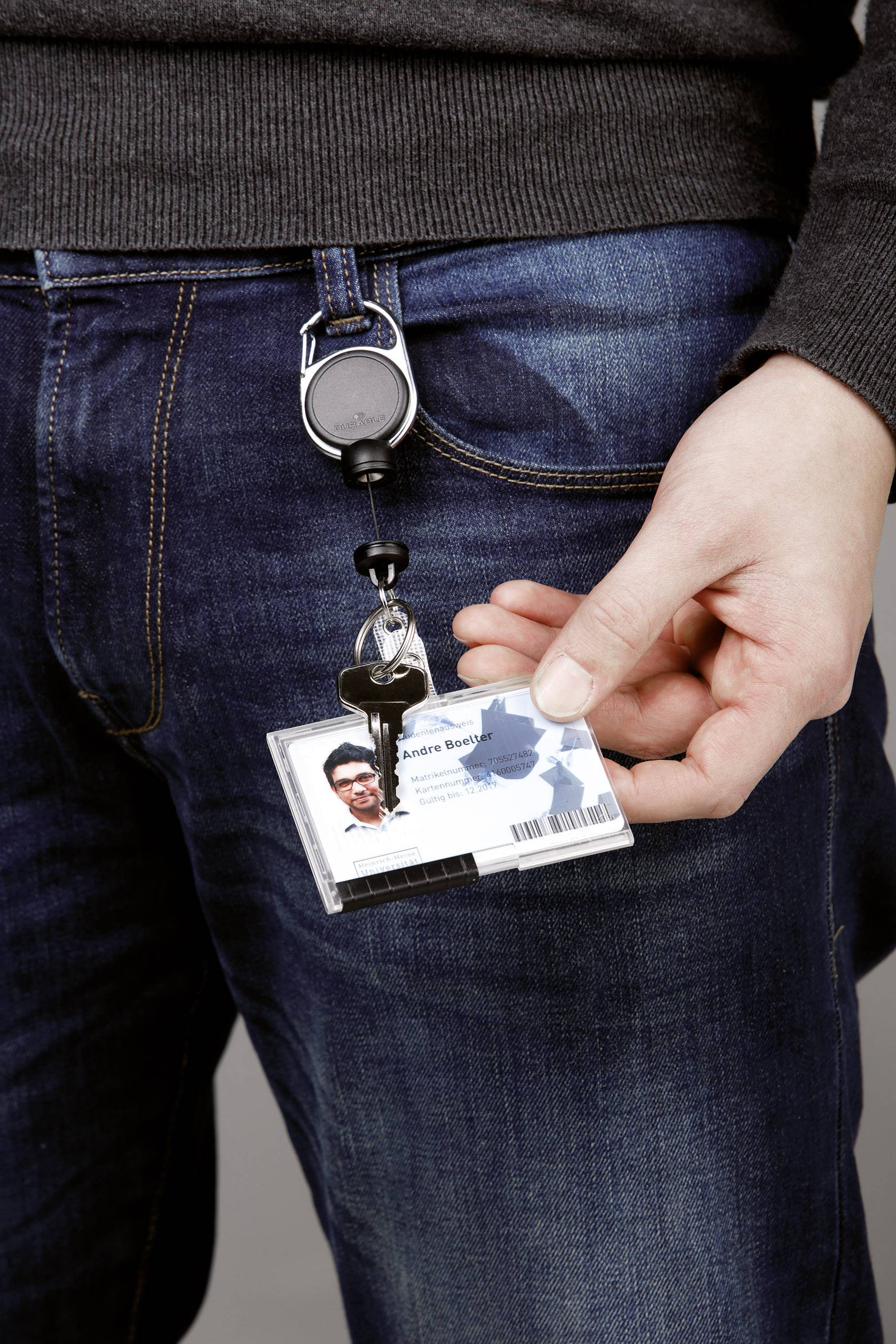 Person hält einen Ausweis mit Foto an einem ausziehbaren Schlüsselanhänger, befestigt an einer Jeanshose.