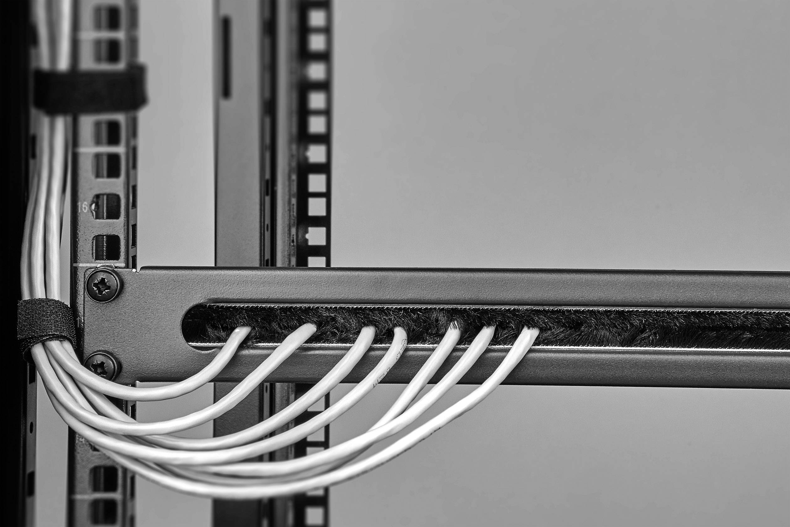 Schwarz-weiß Foto eines Server-Racks mit mehreren Kabeln, die geordnet durch Kabelschlitze verlaufen, zeigt Technikstruktur und Ordnung.