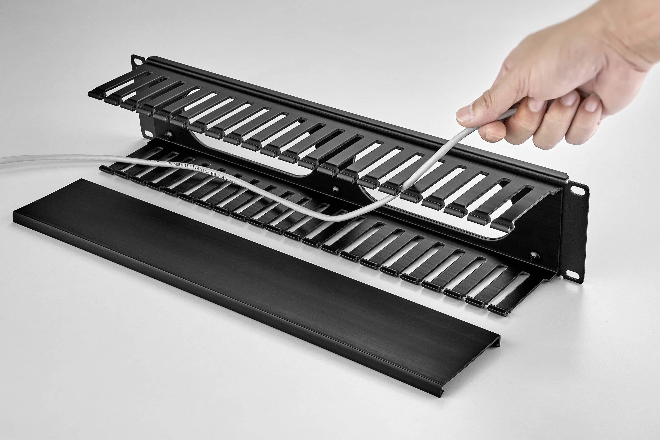 Eine Hand ordnet Kabel in einem schwarzen Kabelmanagementsystem, um Ordnung und Sicherheit in einem technischen oder Bürobereich zu gewährleisten.