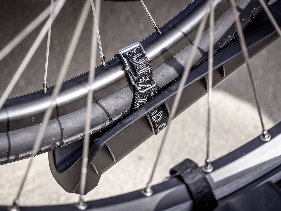 Nahaufnahme eines Fahrradreifens, befestigt an einem Fahrradständer mit einem schwarzen Riemen. Speichen sind ebenfalls sichtbar.