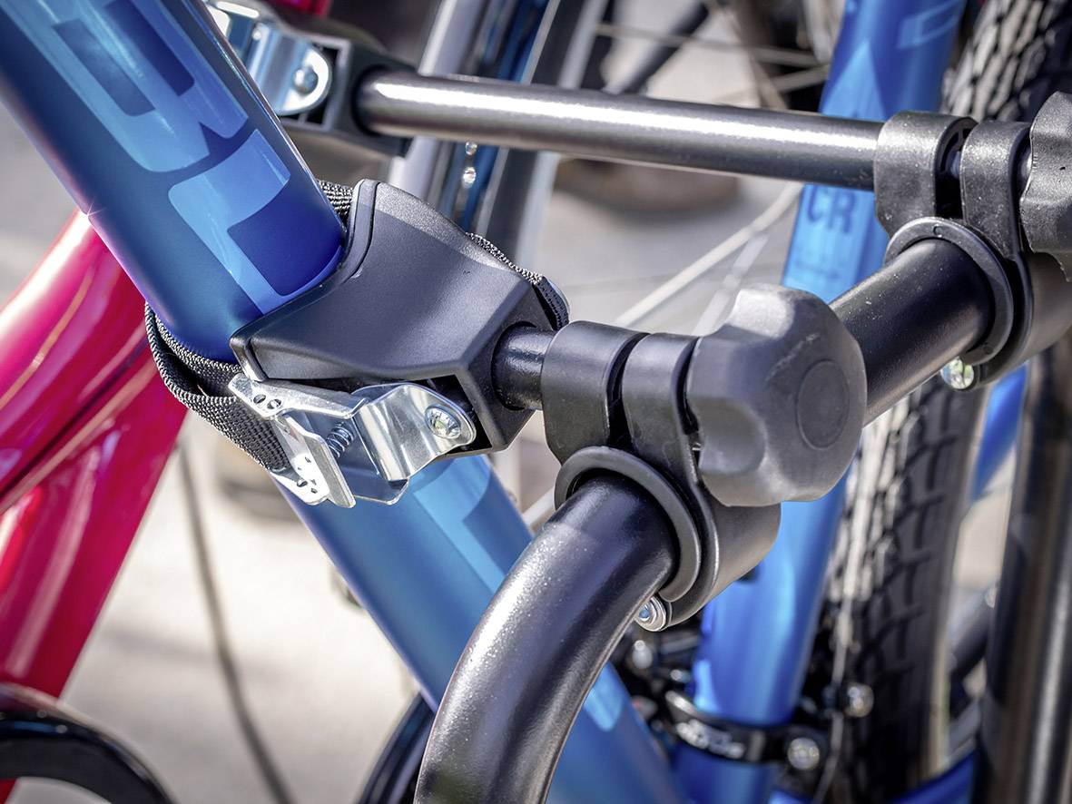 Nahaufnahme eines blau lackierten Fahrradrahmens in einem robusten Sicherheitsschloss. Im Hintergrund ist ein rotes Fahrrad sichtbar.