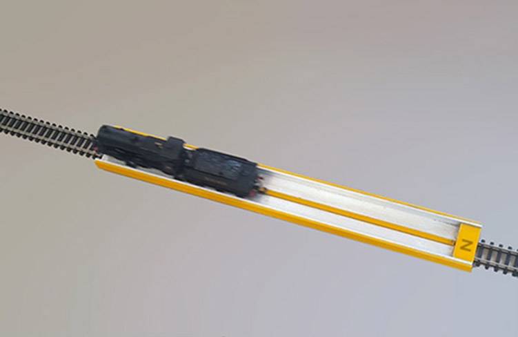 Modellzug auf einer Spur in einem gelben Trog mit der Markierung 'Z', in Bewegung nach rechts dargestellt.