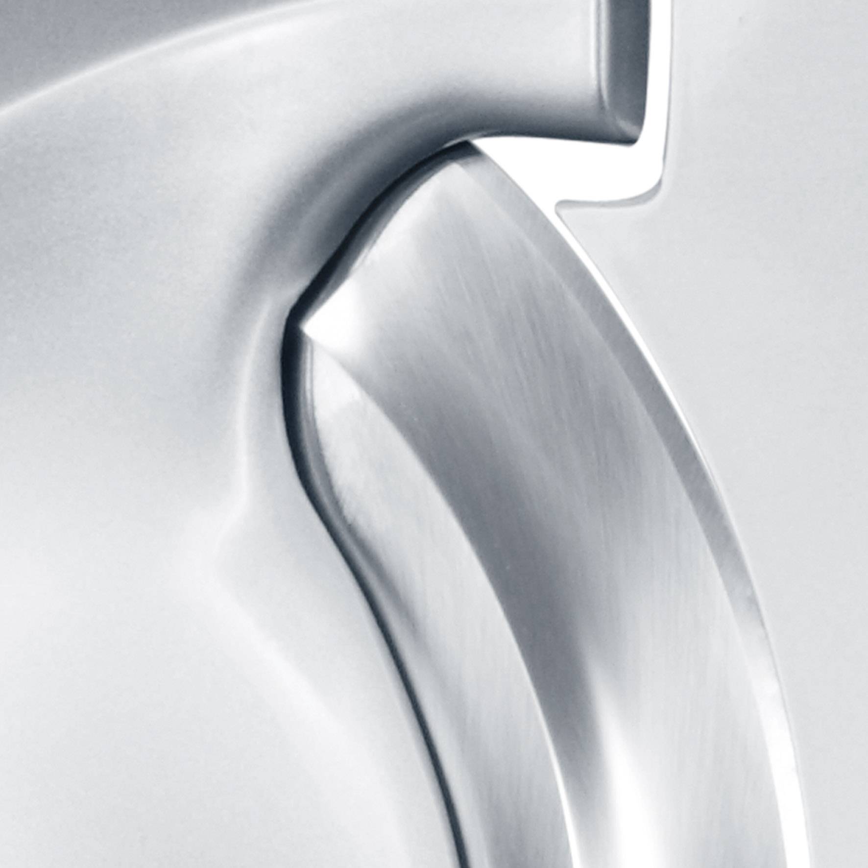 Nahaufnahme eines silbernen, glänzenden Metalloberflächendetails mit glatten Kurven und Kanten, möglicherweise Teil eines Haushaltsgeräts.