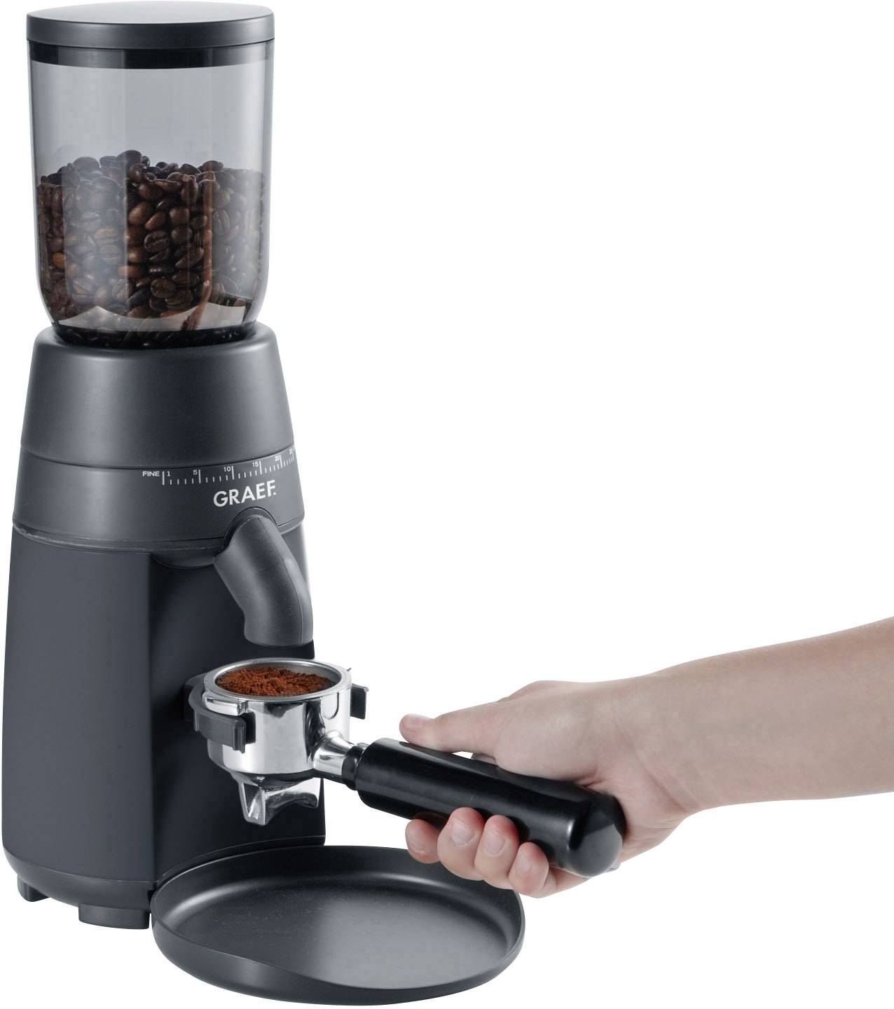 Eine Hand hält einen Kaffeefilter unter der Ausgabedüse einer elektrischen Kaffeemühle mit voller Bohnenkammer.