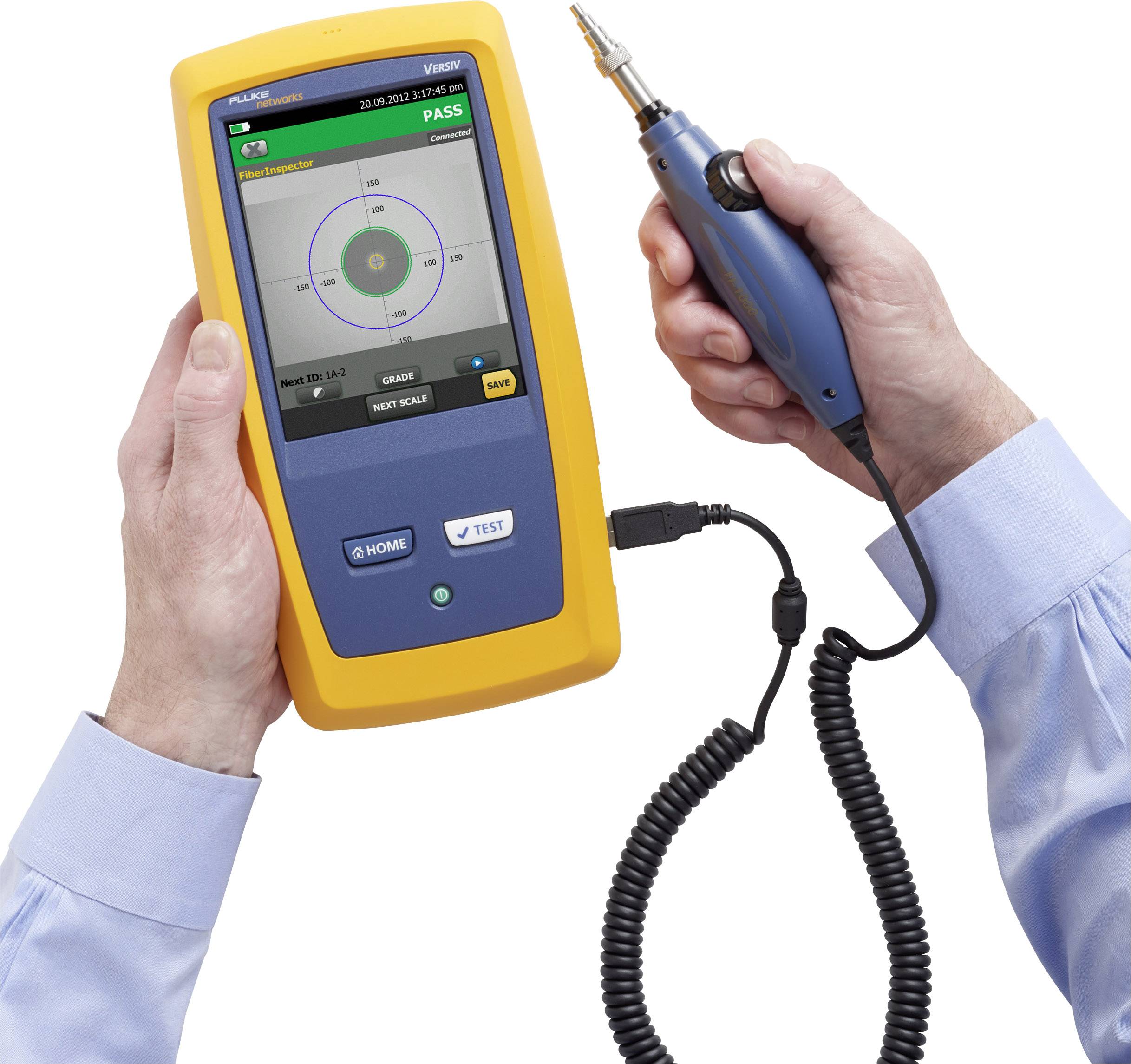 Eine Person hält ein Prüfgerät in gelbem Gehäuse mit Display und einer angeschlossenen blauen Werkzeugsonde, die für Glasfaser-Tests verwendet wird.