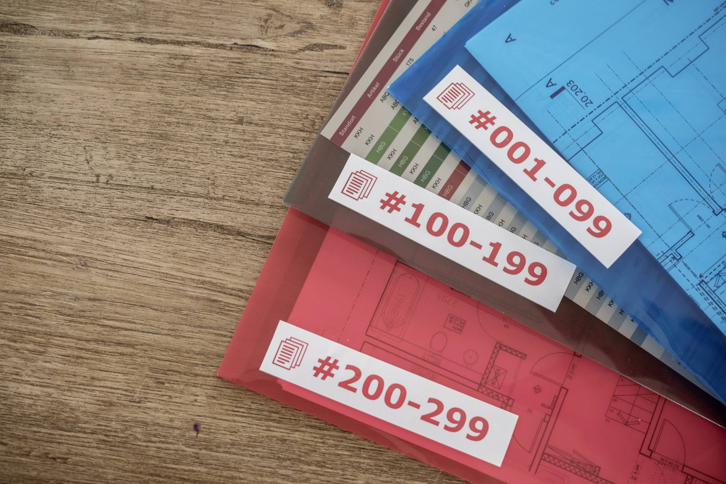 Drei Ordner mit Plänen liegen auf einem Holztisch. Sie sind nummeriert mit '#001-099', '#100-199' und '#200-299'.