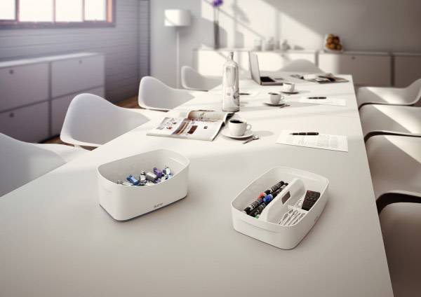 Ein Konferenzraum mit weißen Stühlen. Zwei Organizer mit Stiften und Bürobedarf auf dem Tisch. Helle Fenster im Hintergrund.