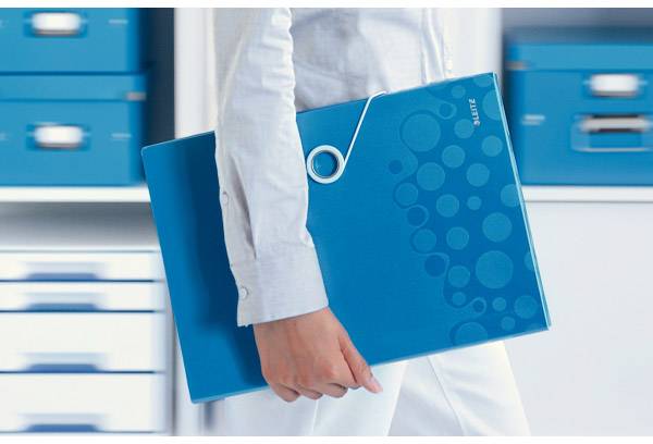 Person hält blauen Ordner, trägt weiße Kleidung und steht vor einem Regal mit blauen Boxen.