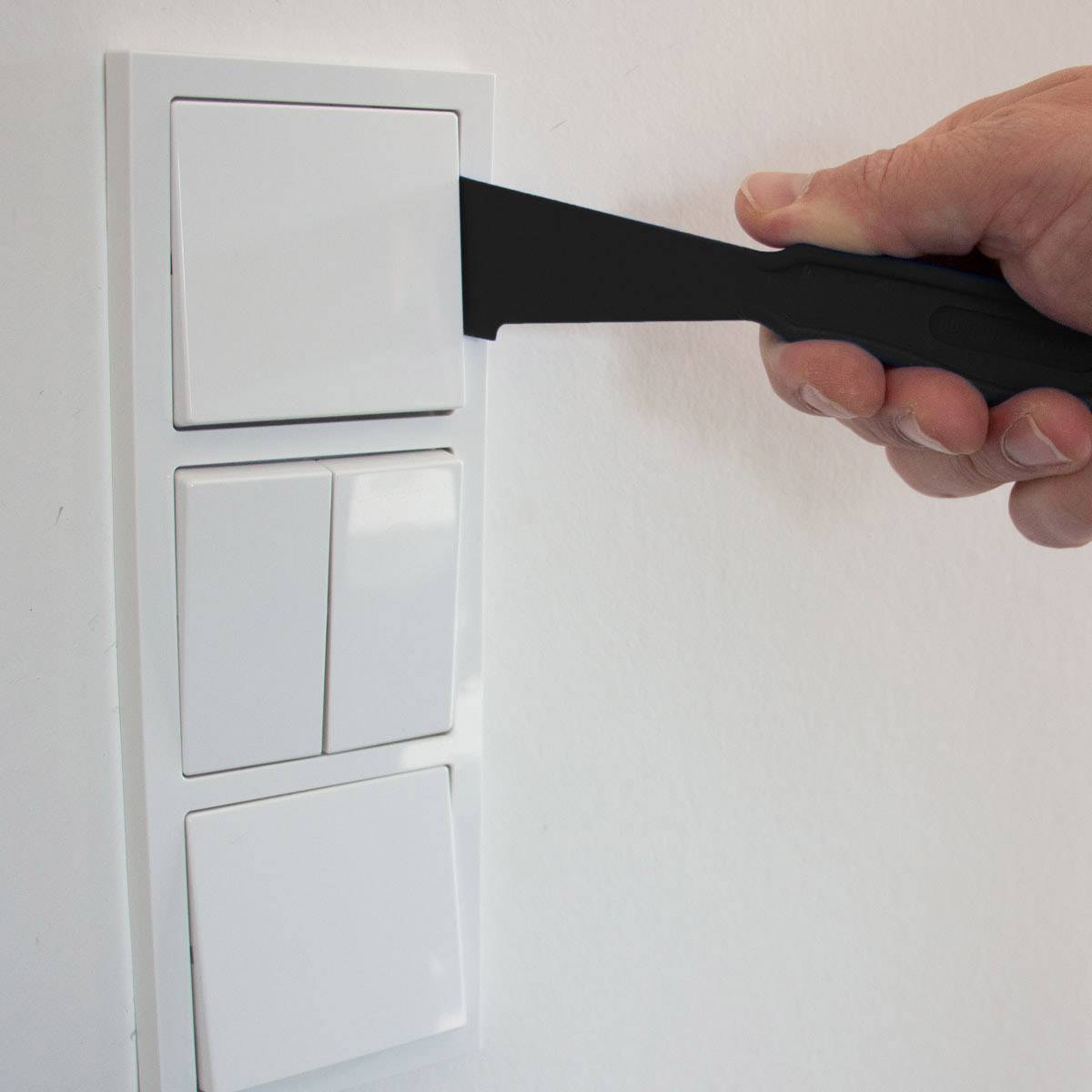 Eine Hand hält ein großes Messer, das zwischen einem Doppellichtschalter steckt.