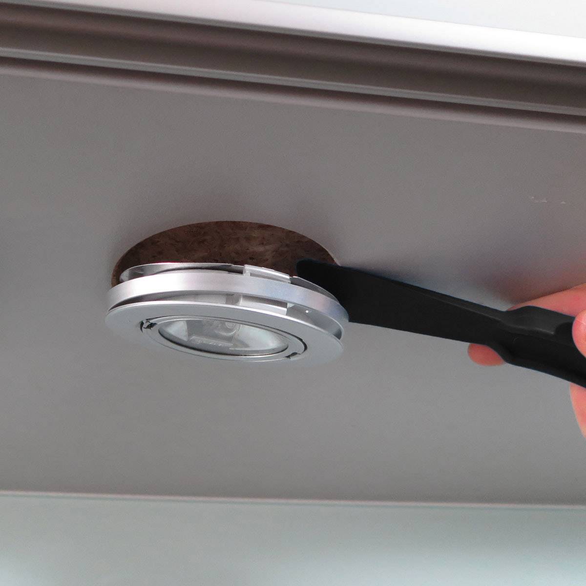 Eine Person entfernt mit einem flachen Werkzeug ein rundes LED-Licht aus einer Deckenhalterung.