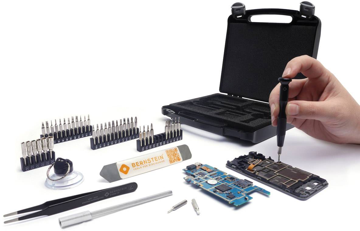 Eine Hand verwendet einen Schraubendreher, um an einer offenen elektronischen Platine zu arbeiten. Werkzeug und Bits sind organisiert daneben platziert.