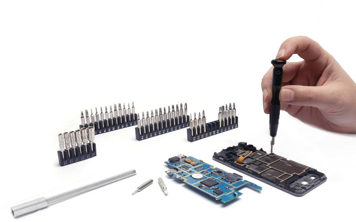 Eine Hand repariert ein Smartphone mit einem Schraubendreher. Daneben liegen diverse Schraubenzieherköpfe und ein offenes Handy-Mainboard.