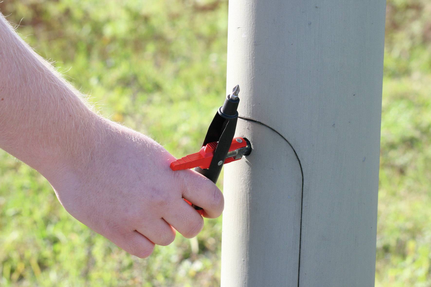 Eine Hand verwendet ein Werkzeug, um einen Schraubendreher an einer Metallkonstruktion im Freien zu befestigen.