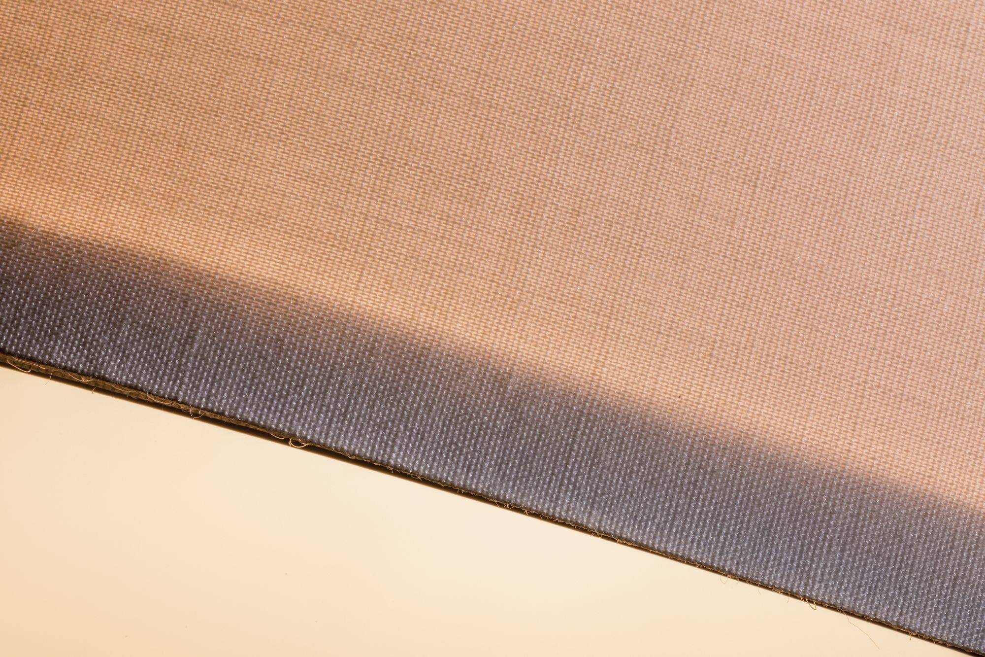 Eine Nahaufnahme eines zweifarbigen Stoffes. Der untere Teil ist dunkel, der obere heller. Es zeigt die Textur und den Farbverlauf.