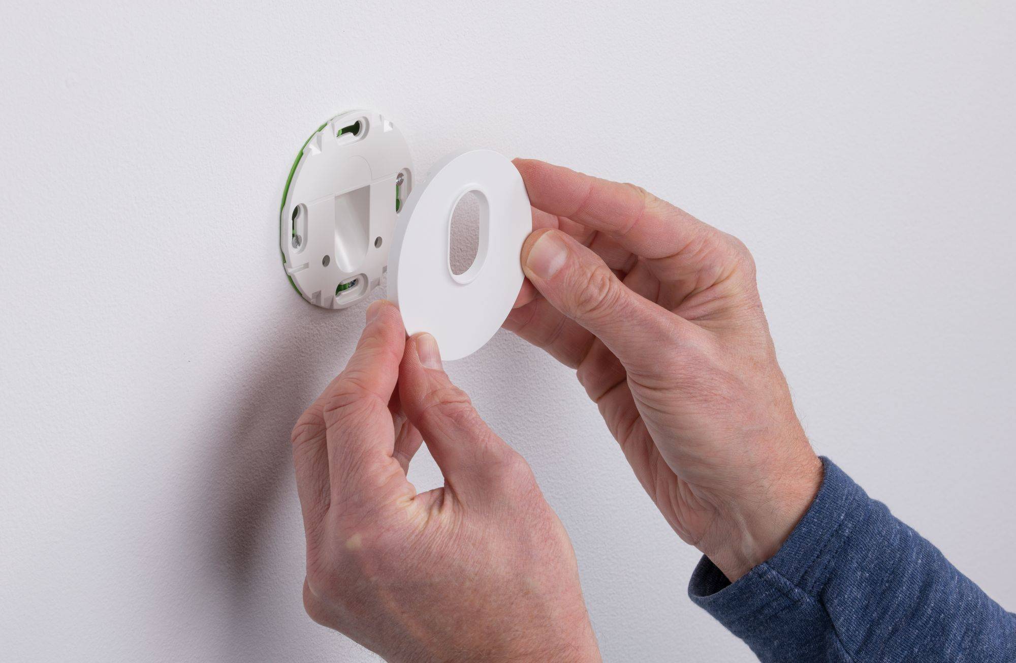 Person befestigt eine runde Abdeckung an einer Wandhalterung, möglicherweise für ein Thermostat oder ein ähnliches Gerät.