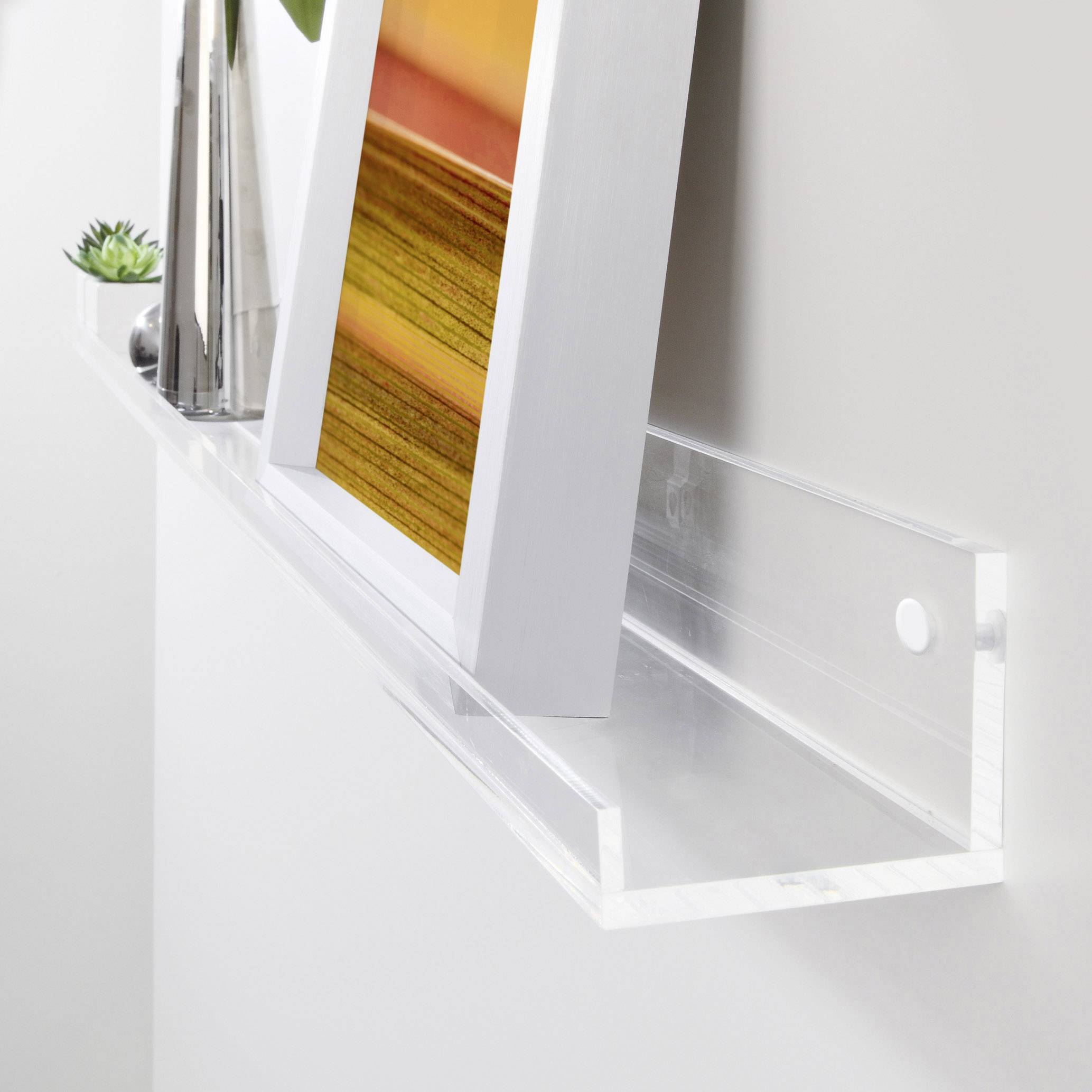 Acrylregal an der Wand mit schwebendem Fotorahmen und Dekoration, darunter eine Vase und eine kleine Pflanze.