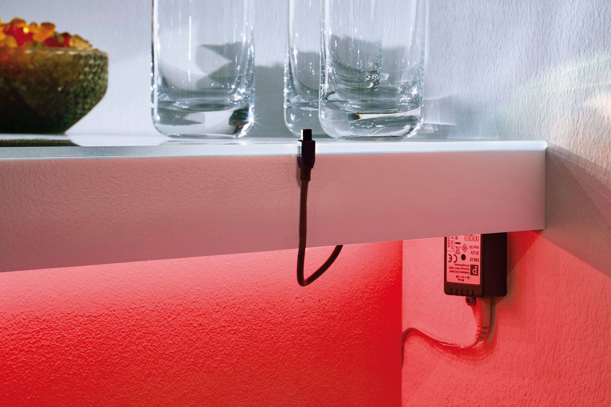 Ein Regal mit Gläsern und einer Schale, darunter ein herausragendes Kabel von einem LED-Transformator. Der Hintergrund ist rot beleuchtet.