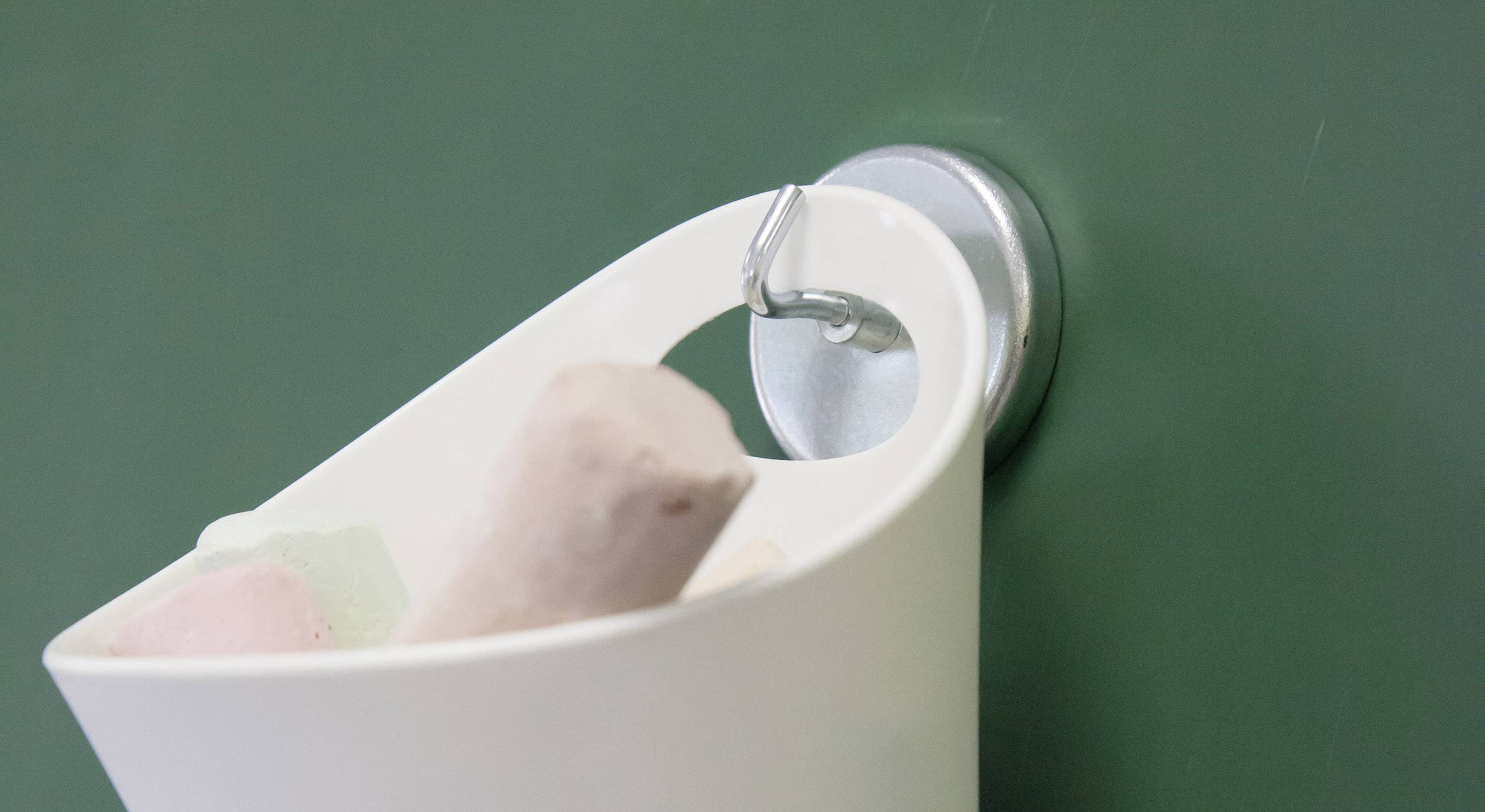 Kleiner weißer Eimer mit bunten Kreiden hängt an einem Haken vor einer grünen Tafel.