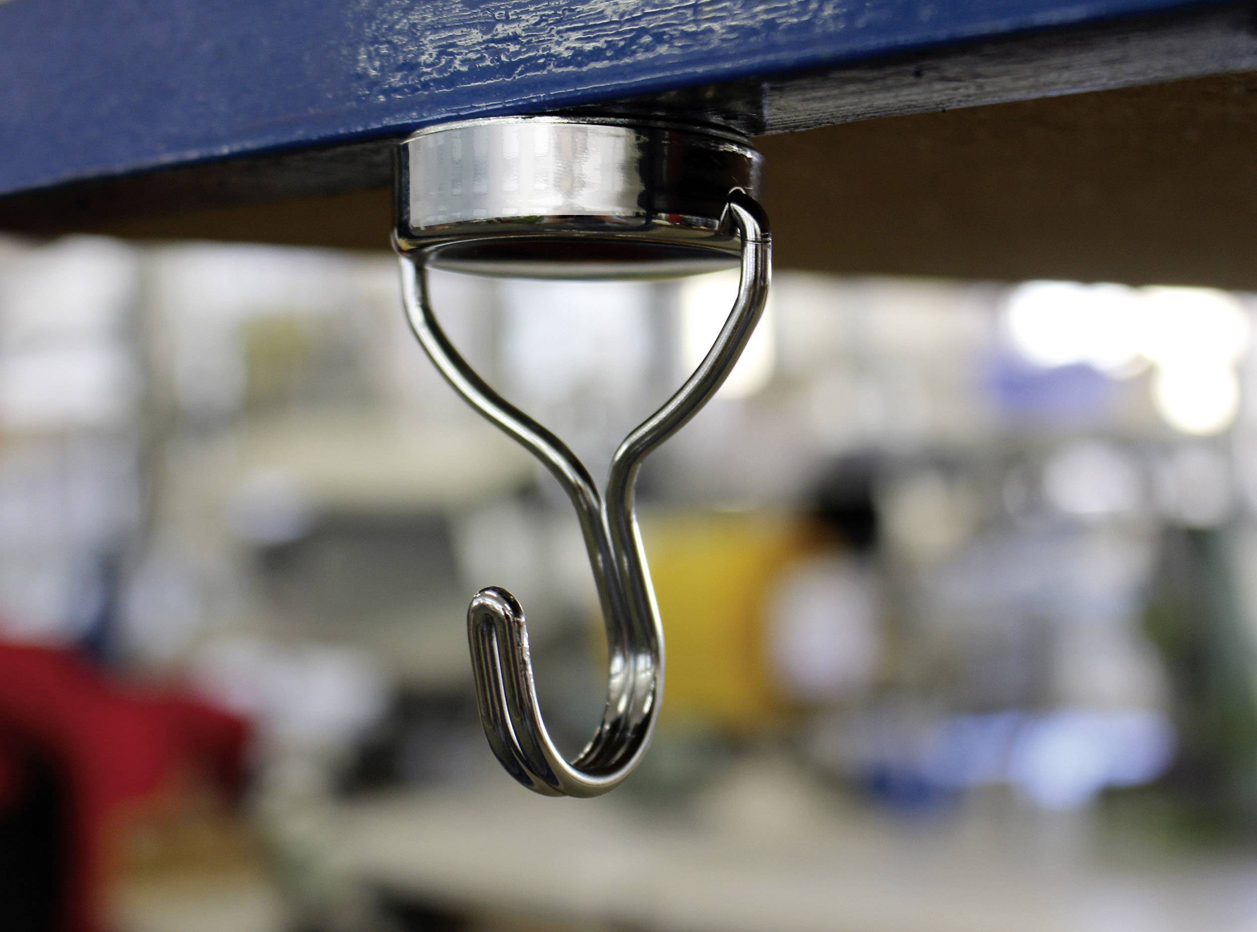 Metallhaken unter einem Tisch, dient zur Aufbewahrung oder zum Aufhängen von Gegenständen in einem Arbeitsumfeld. Hintergrund unscharf.