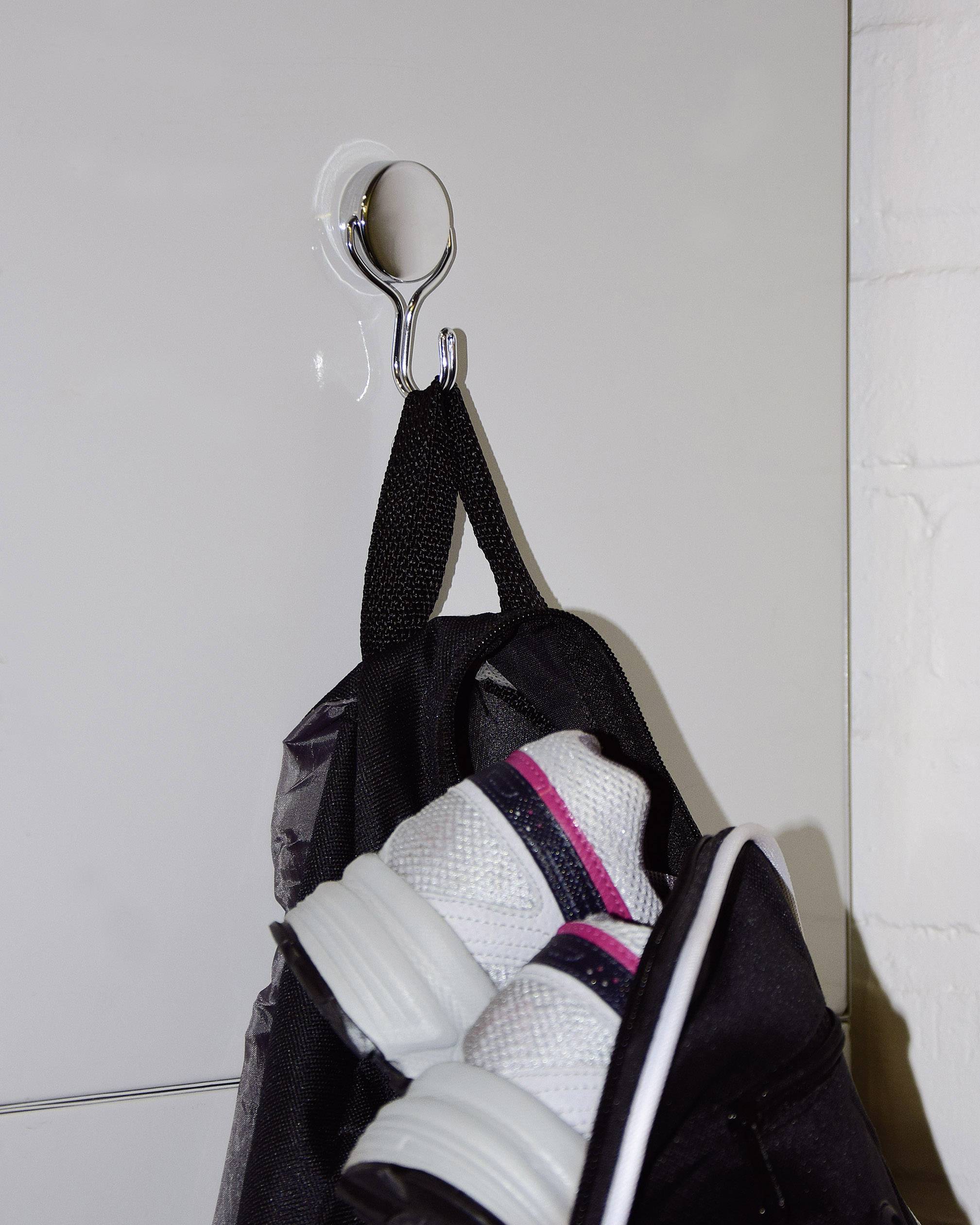 Ein schwarzer Rucksack hängt an einem Haken. Weiße Turnschuhe mit rosa Streifen ragen aus dem Rucksack heraus.