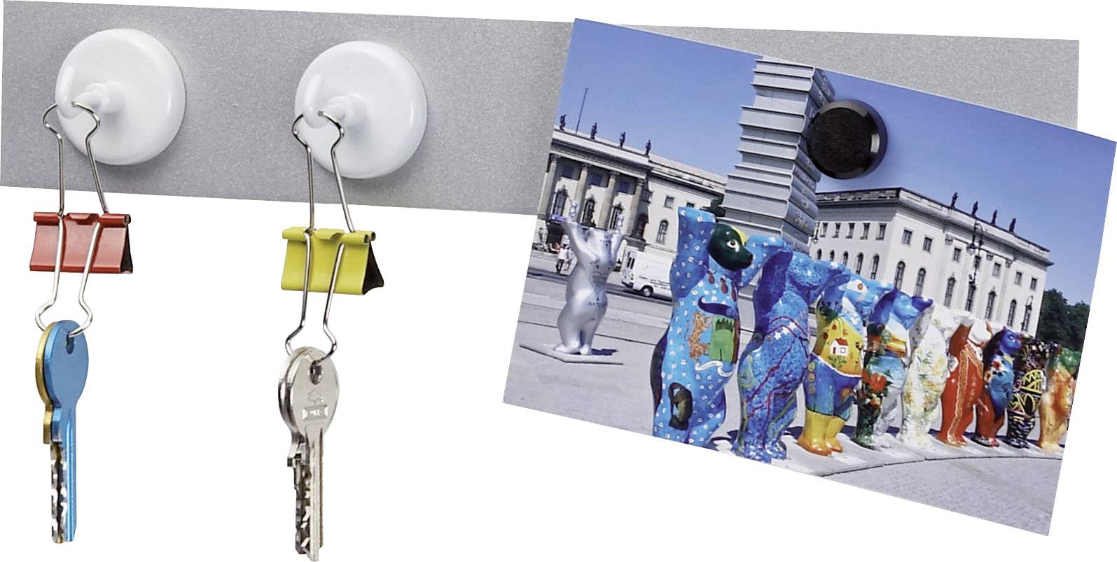 Zwei Schlüssel hängen an farbigen Klammern an Magneten, daneben eine Postkarte mit bemalten Bärenfiguren vor einem historischen Gebäude.