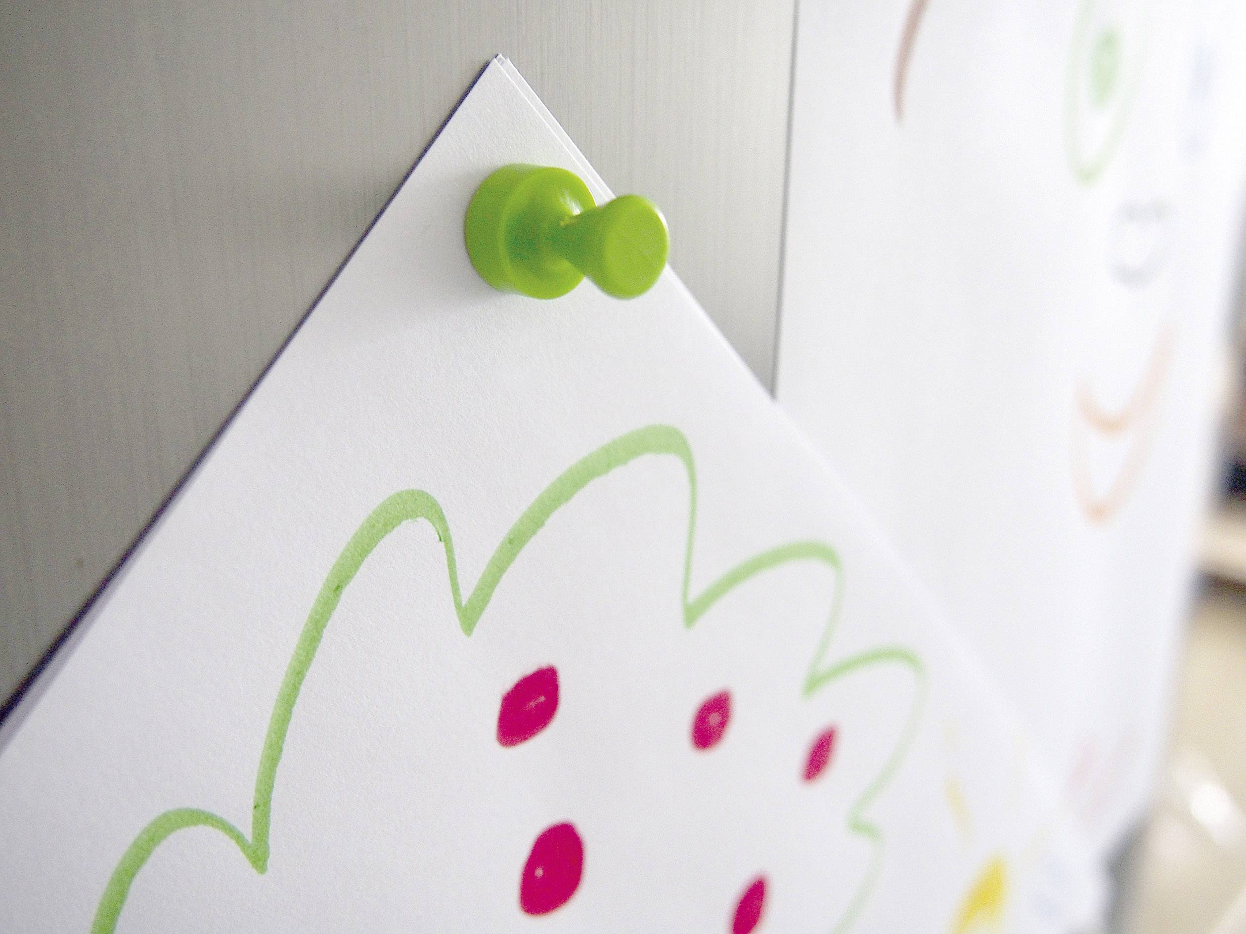 Eine Zeichnung mit roten Punkten und grünen Linien ist mit einem grünen Reißnagel an eine metallische Oberfläche geheftet.