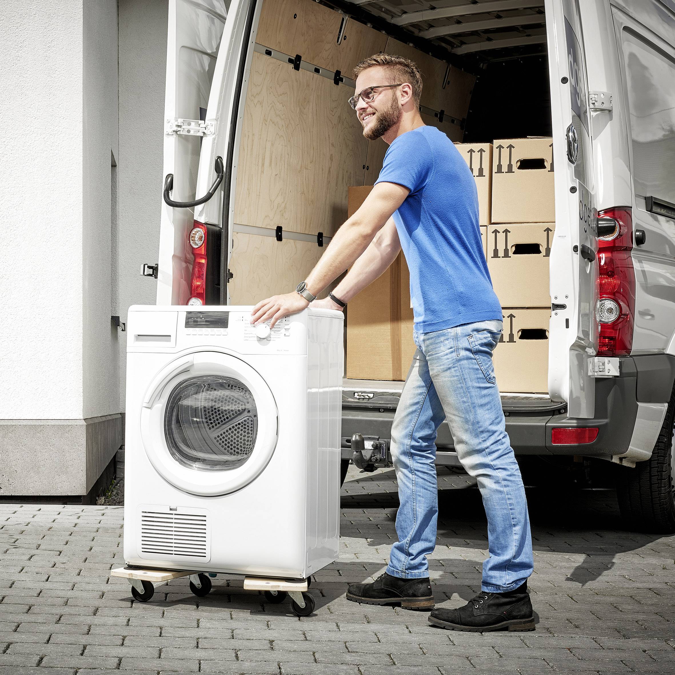 Ein Mann in blauem T-Shirt hebt eine Waschmaschine aus einem Lieferwagen voller Kartons.