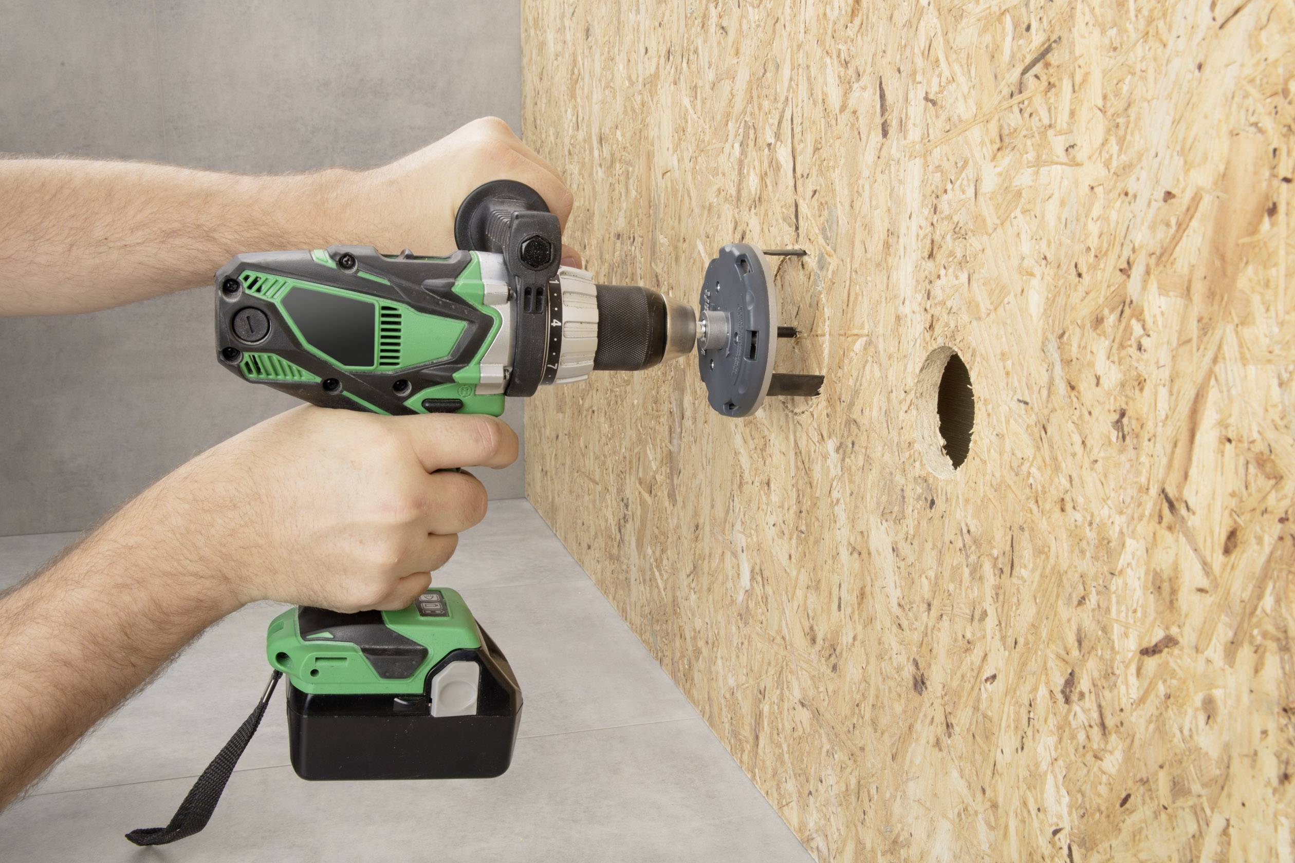 Eine Person verwendet eine grüne Bohrmaschine, um ein Loch in eine Sperrholzplatte zu bohren.