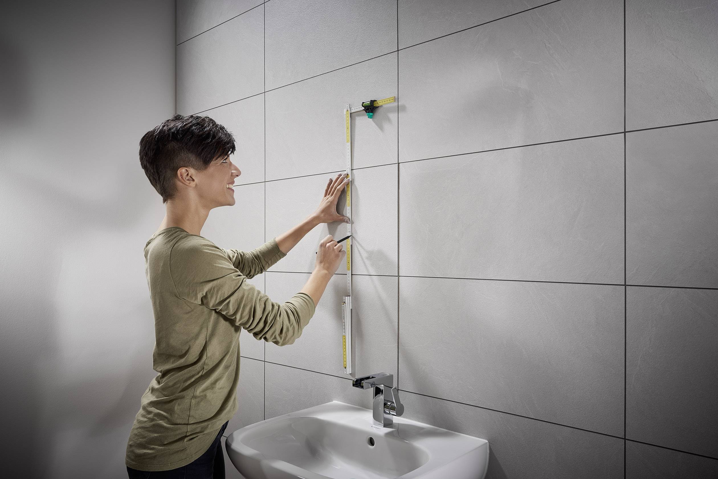 Eine Person misst eine Wand über einem Waschbecken mit einem Lineal und einer Wasserwaage.
