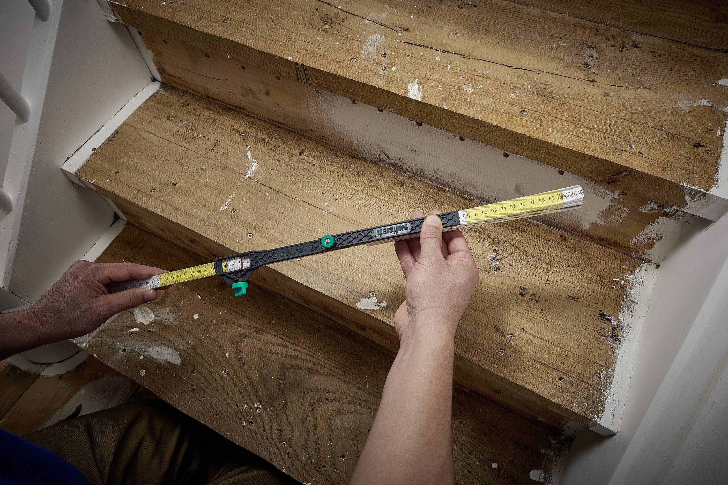 Eine Person misst die Breite einer Holzstufe mit einem Messgerät, um Renovierungsarbeiten durchzuführen.