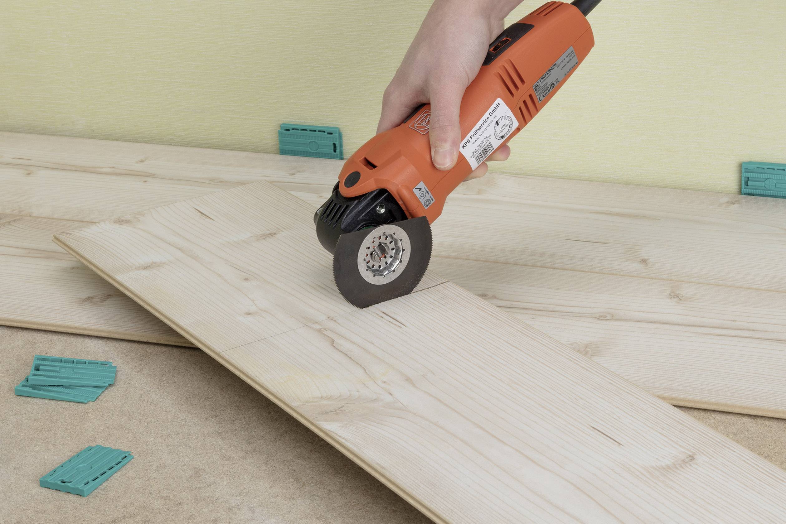 Eine Person schneidet mit einem oszillierenden Multifunktionswerkzeug ein Holzbrett. Im Hintergrund liegen weitere Holzplanken.