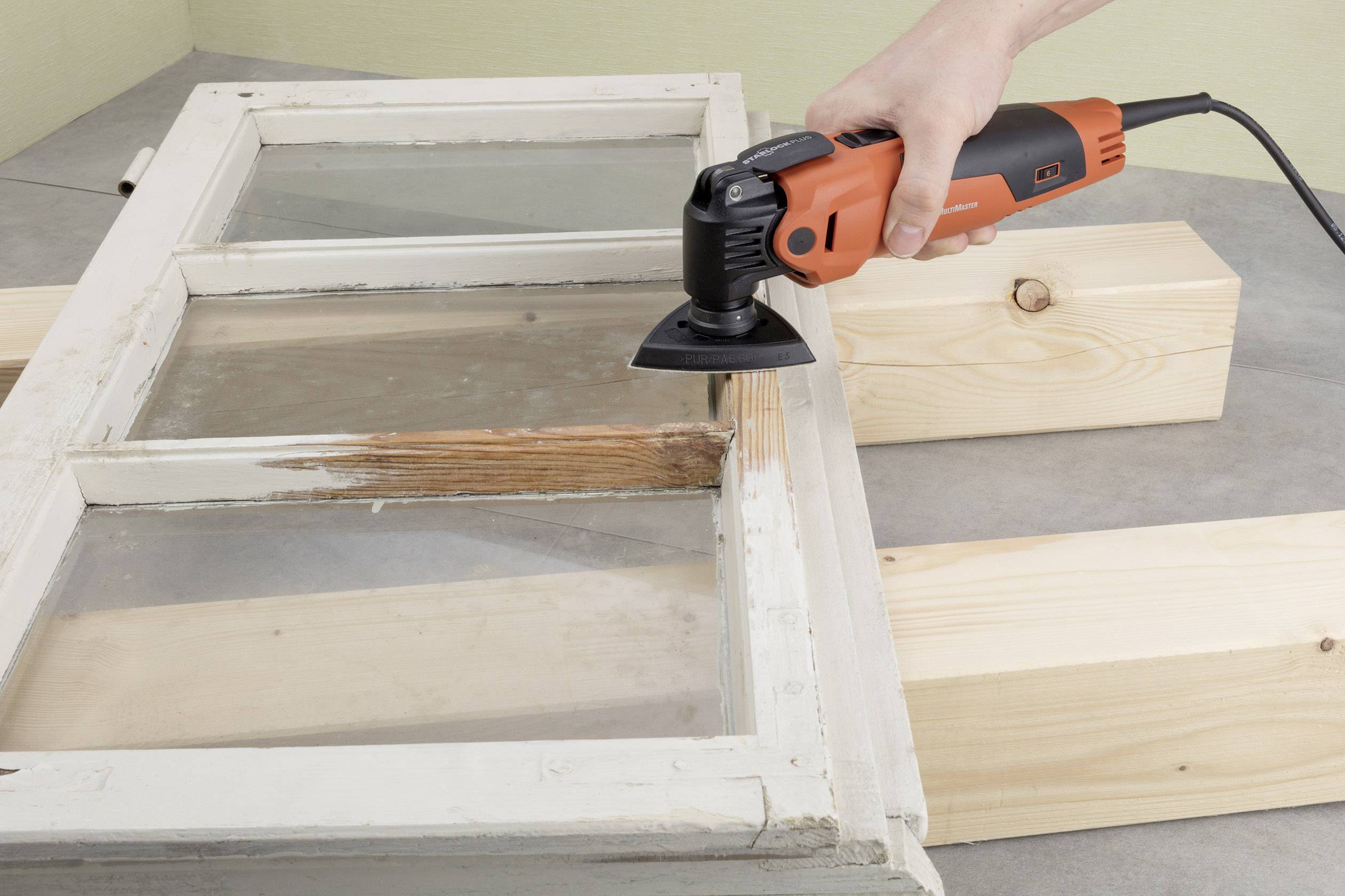 Eine Person schleift mit einem elektrischen Schleifgerät Farbe von einem alten Holzfensterrahmen ab.