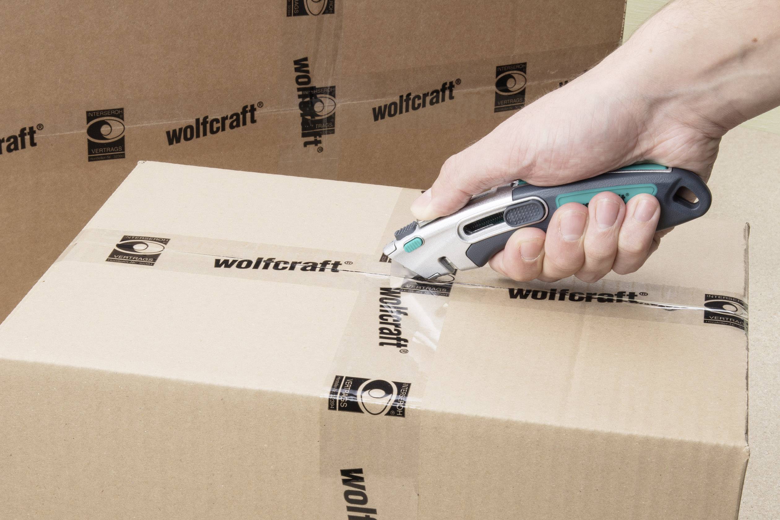 Eine Hand benutzt ein Cuttermesser, um Klebeband von einem Karton mit 'wolfcraft'-Logo zu schneiden.