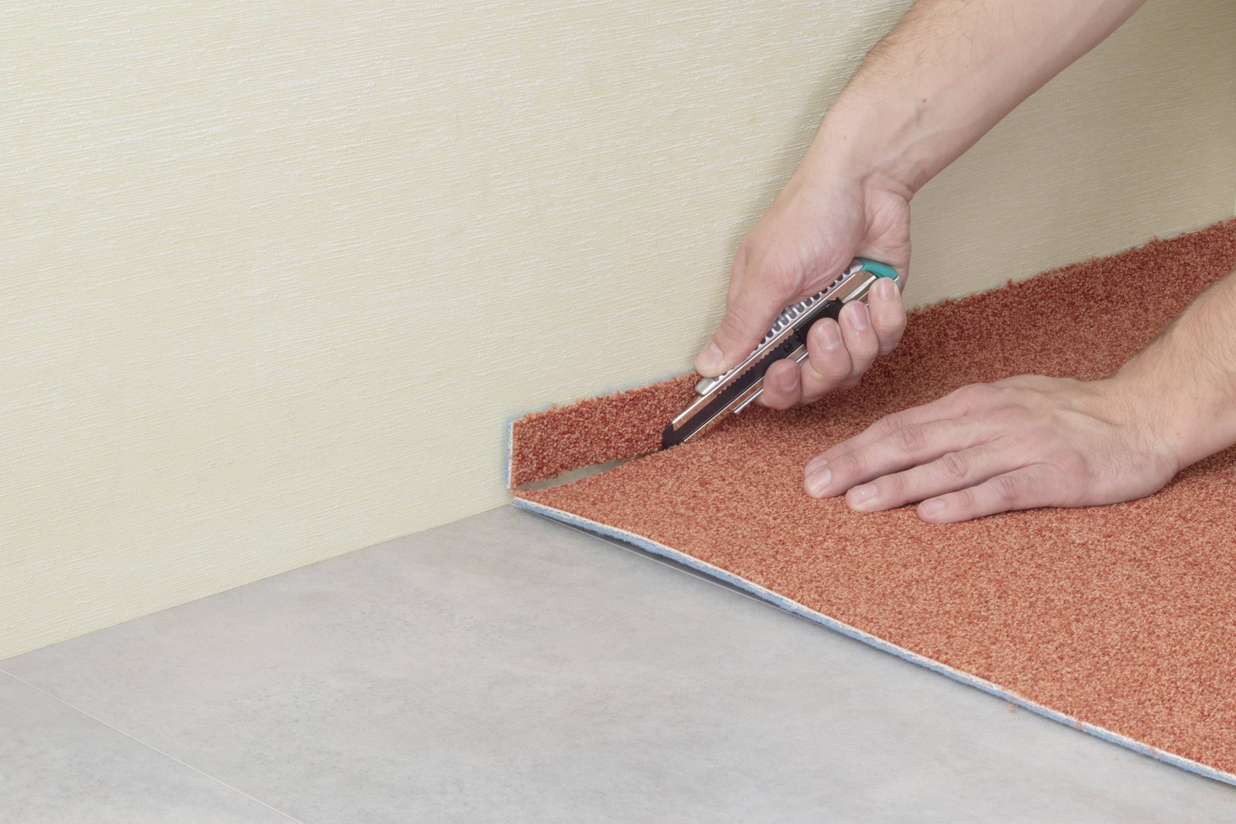 Ein Teppich wird mit einem Teppichmesser entlang der Wand auf die passende Größe zugeschnitten.